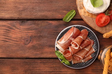 Rolled slices of delicious jamon and different products on wooden table, flat lay. Space for text