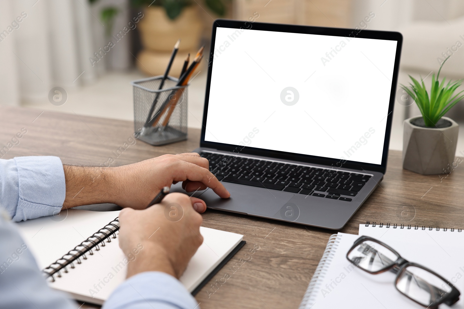 Photo of E-learning. Young man using laptop at wooden table indoors, closeup