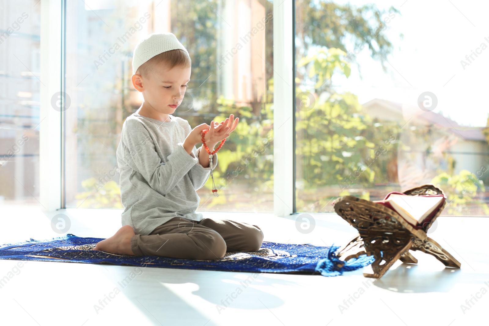 Photo of Little Muslim boy with misbaha and Koran praying on rug indoors