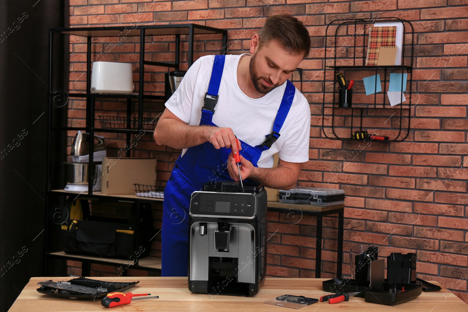 Photo of Repairman with screwdriver fixing coffee machine at table indoors