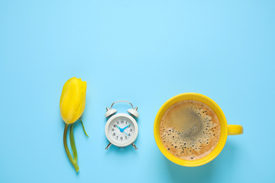Delicious morning coffee, alarm clock and tulip on light blue background, flat lay. Space for text
