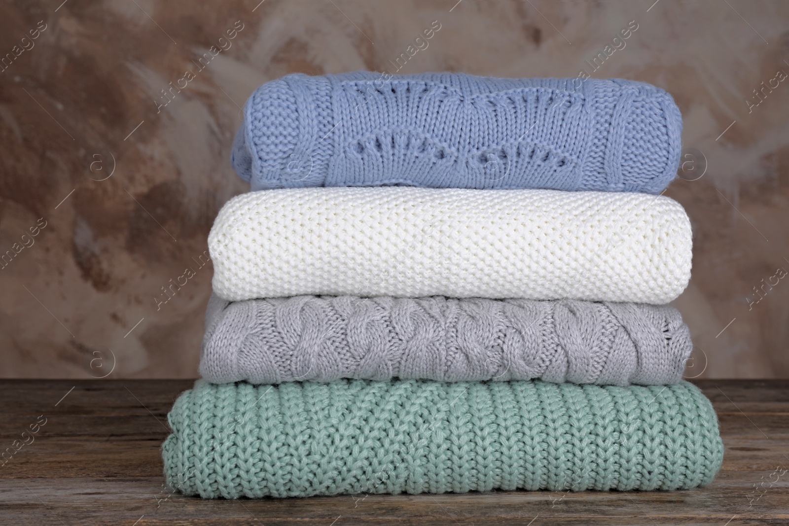 Photo of Stack of folded knitted sweaters on wooden table against brown background