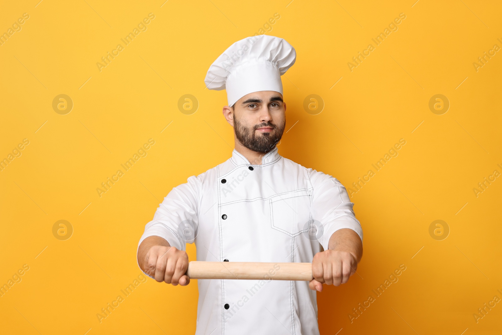 Photo of Professional chef with rolling pin on yellow background