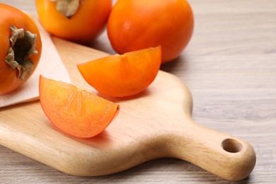 Photo of Delicious ripe persimmons on light wooden table, closeup