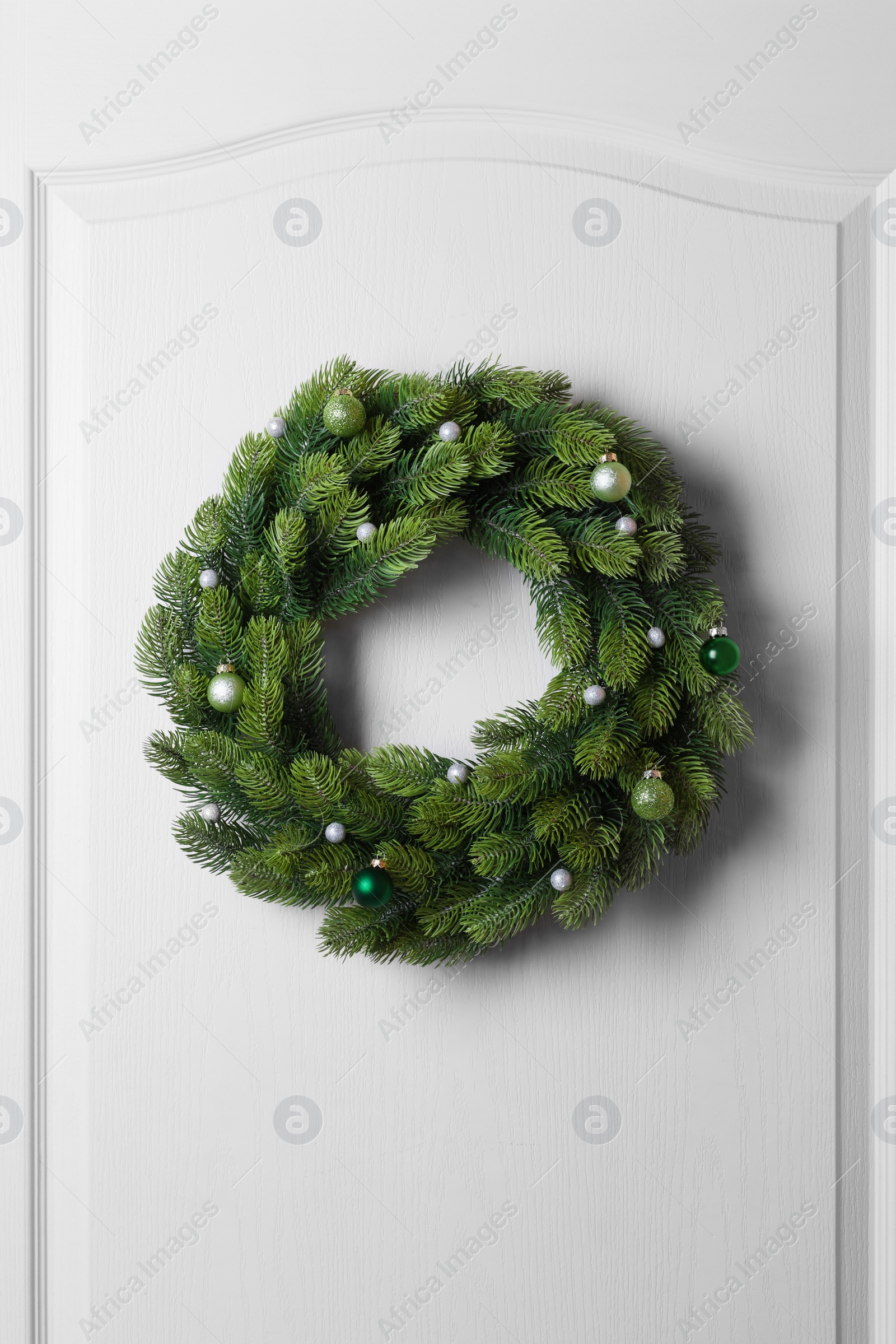 Photo of Beautiful Christmas wreath with festive decor hanging on white door