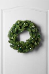 Beautiful Christmas wreath with festive decor hanging on white door