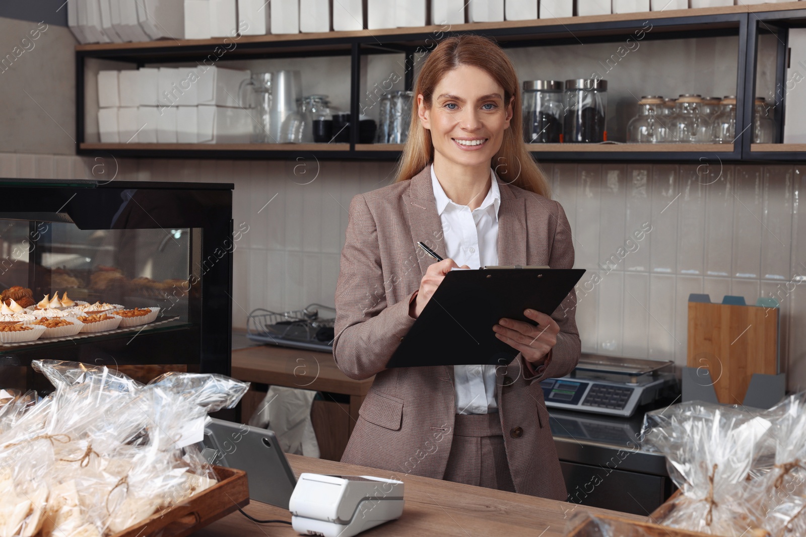 Photo of Happy business owner with clipboard and pen at cashier desk in bakery shop