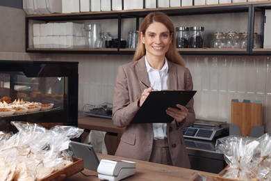 Photo of Happy business owner with clipboard and pen at cashier desk in bakery shop