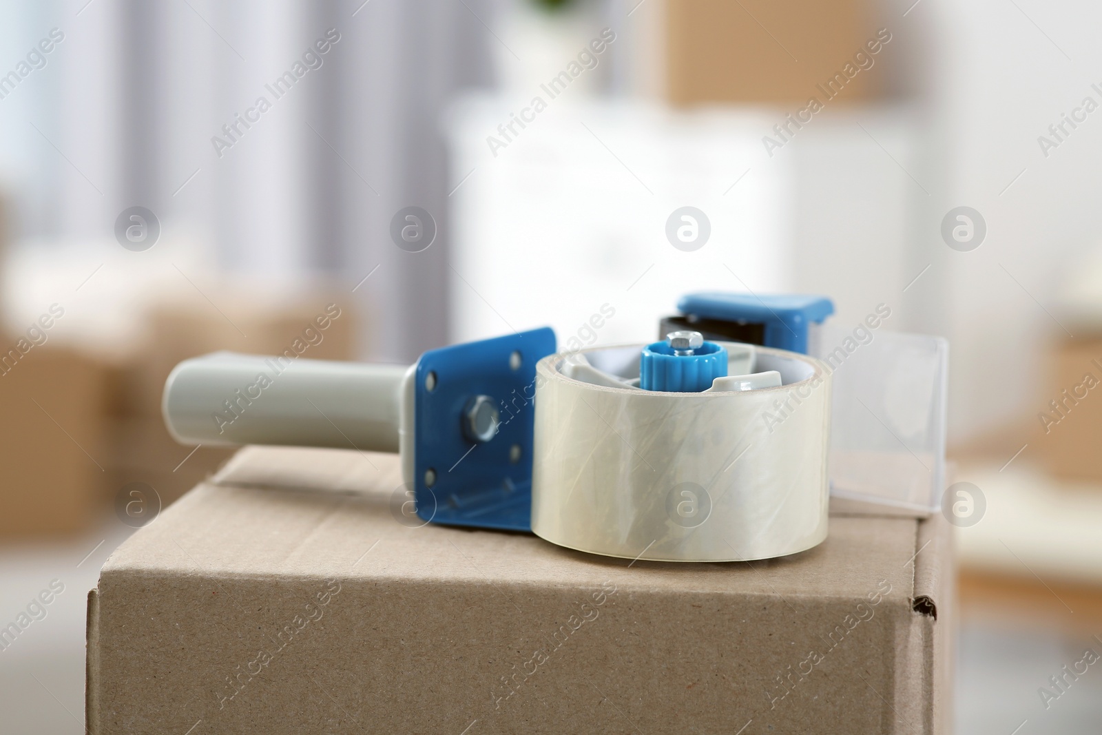 Photo of Dispenser with roll of adhesive tape on box indoors, closeup