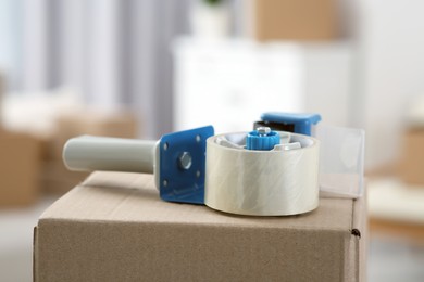 Photo of Dispenser with roll of adhesive tape on box indoors, closeup