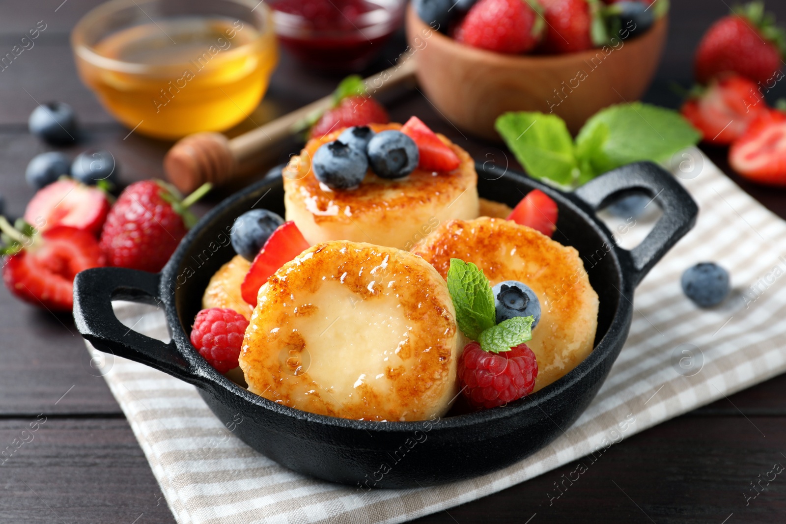 Photo of Delicious cottage cheese pancakes with fresh berries and honey on wooden table, closeup