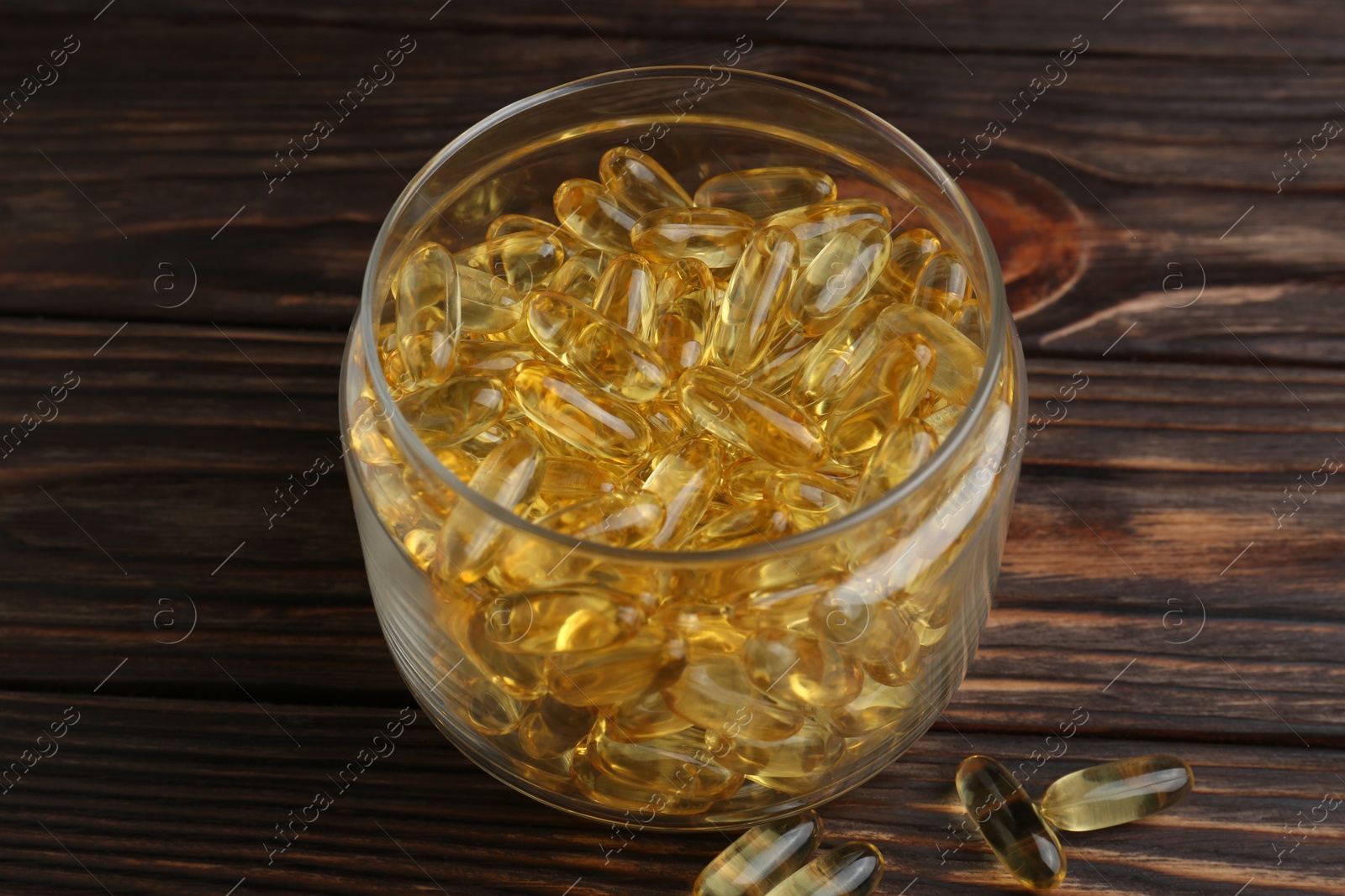 Photo of Glass medical bottle with yellow capsules on wooden table, closeup