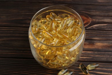 Photo of Glass medical bottle with yellow capsules on wooden table, closeup