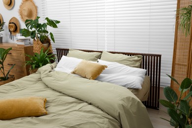 Comfortable bed and beautiful green houseplants in bedroom