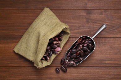 Photo of Metal scoop and sack with dry kidney beans on wooden table, flat lay