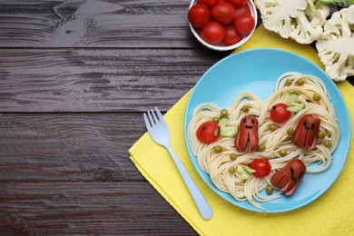 Photo of Creative serving for kids. Plate with cute octopuses madesausages, pasta and vegetables on wooden table, flat lay. Space for text