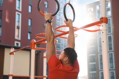 Photo of Man training on gymnastic rings at outdoor gym on sunny day
