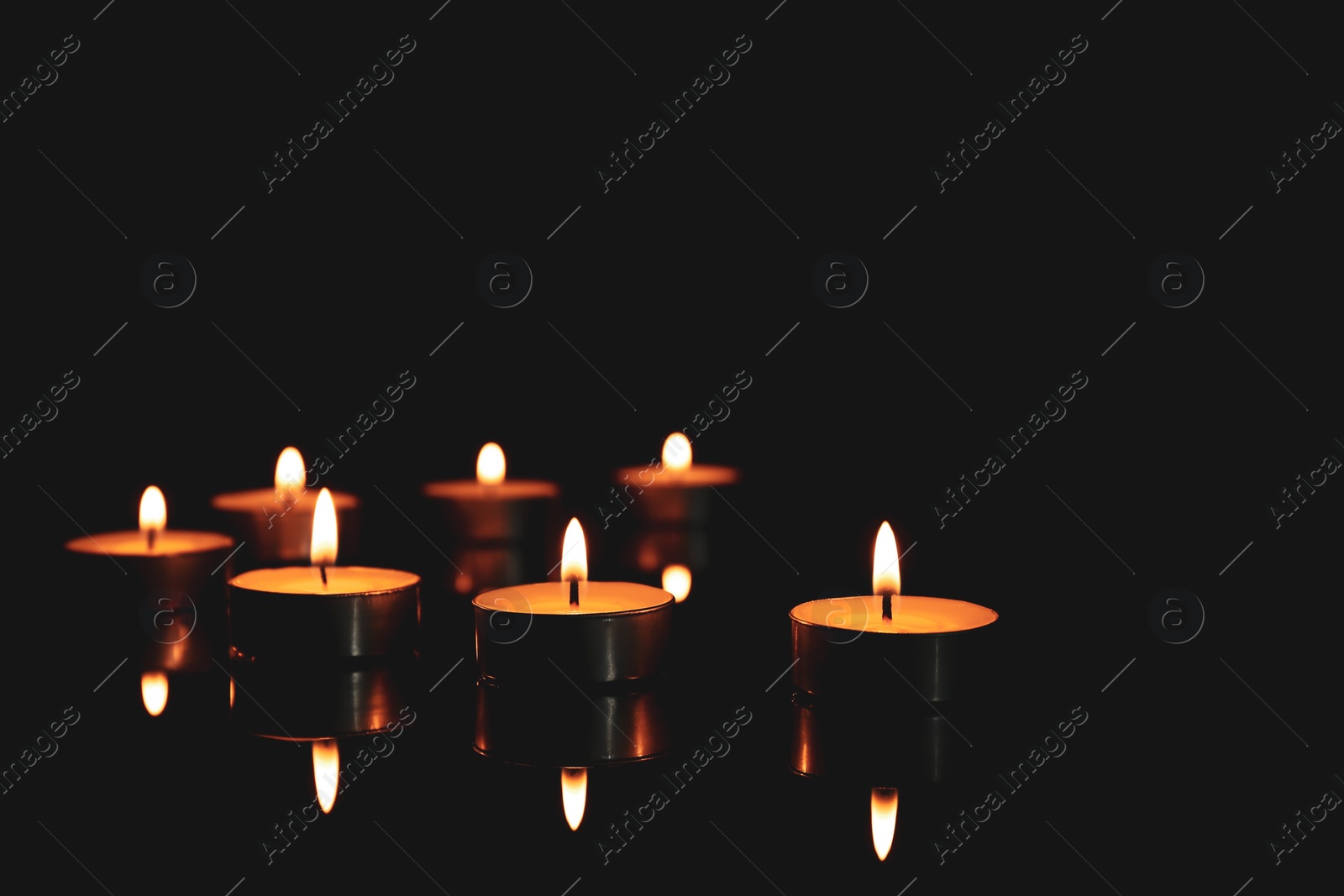 Photo of Burning candles in holders on table against dark background, space for text