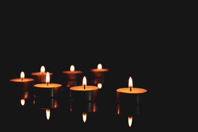 Burning candles in holders on table against dark background, space for text