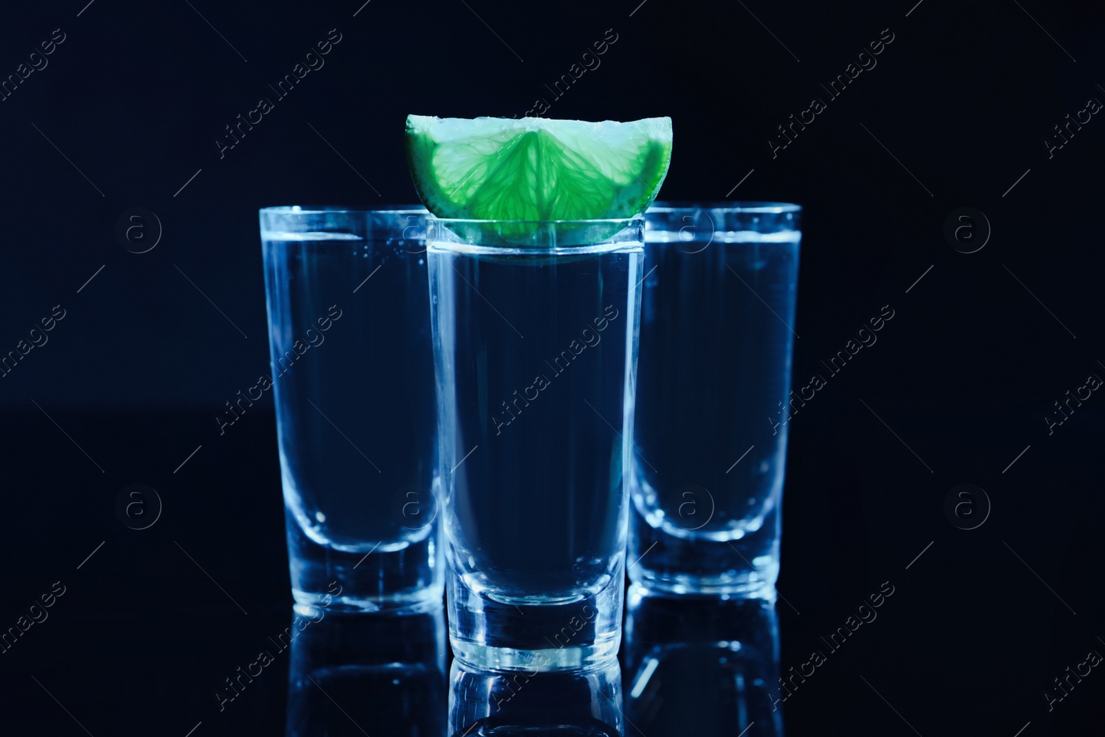 Photo of Shot glasses of vodka with lime slice on dark background