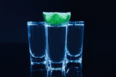 Shot glasses of vodka with lime slice on dark background