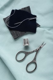 Photo of Thimble, needle and scissors on green cloth, flat lay. Sewing accessories