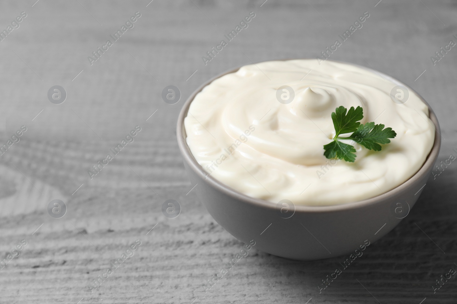 Photo of Tasty mayonnaise and parsley in bowl on gray wooden table, closeup. Space for text