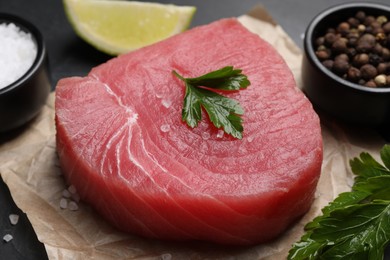 Raw tuna fillet with parsley and spices on table, closeup