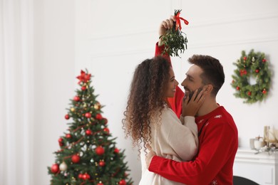 Lovely couple under mistletoe bunch in room decorated for Christmas