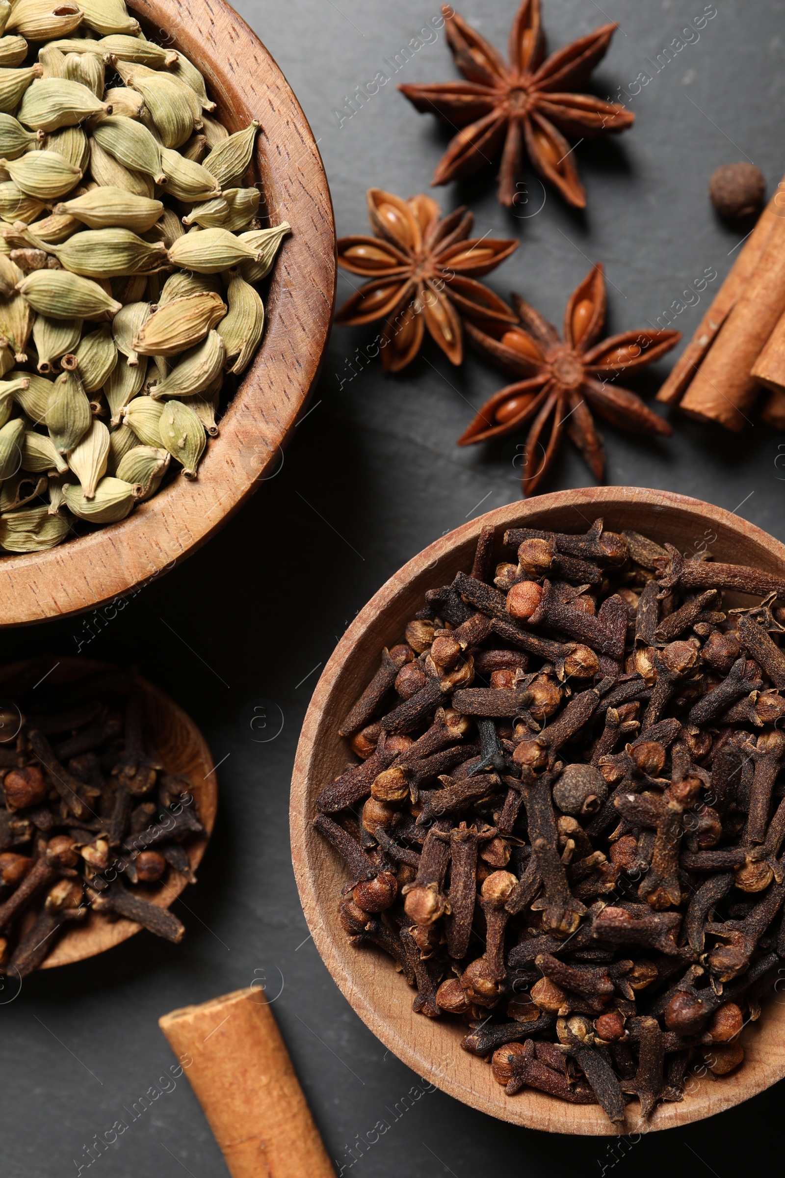 Photo of Different spices in bowls on dark gray textured table, flat lay