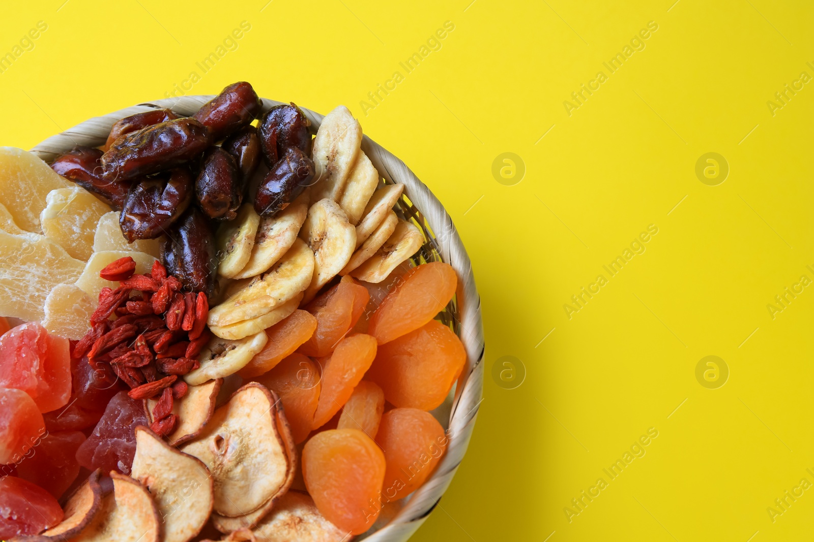 Photo of Wicker basket with different dried fruits on yellow background, closeup. Space for text