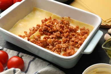 Photo of Cooking lasagna. Pasta sheets, minced meat in baking tray and tomato on table, closeup