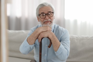 Portrait of grandpa with glasses and walking cane on sofa indoors