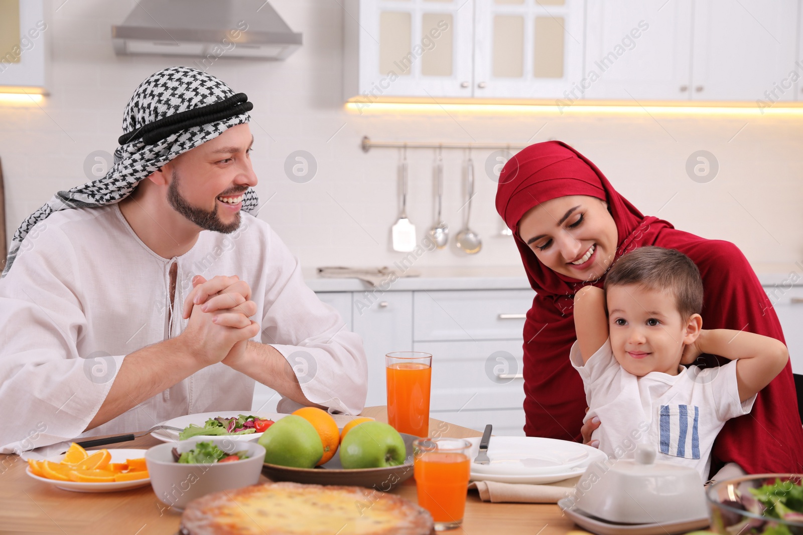 Photo of Happy Muslim family eating together at table in kitchen