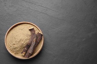 Powder in bowl and dried sticks of liquorice root on black table, top view. Space for text