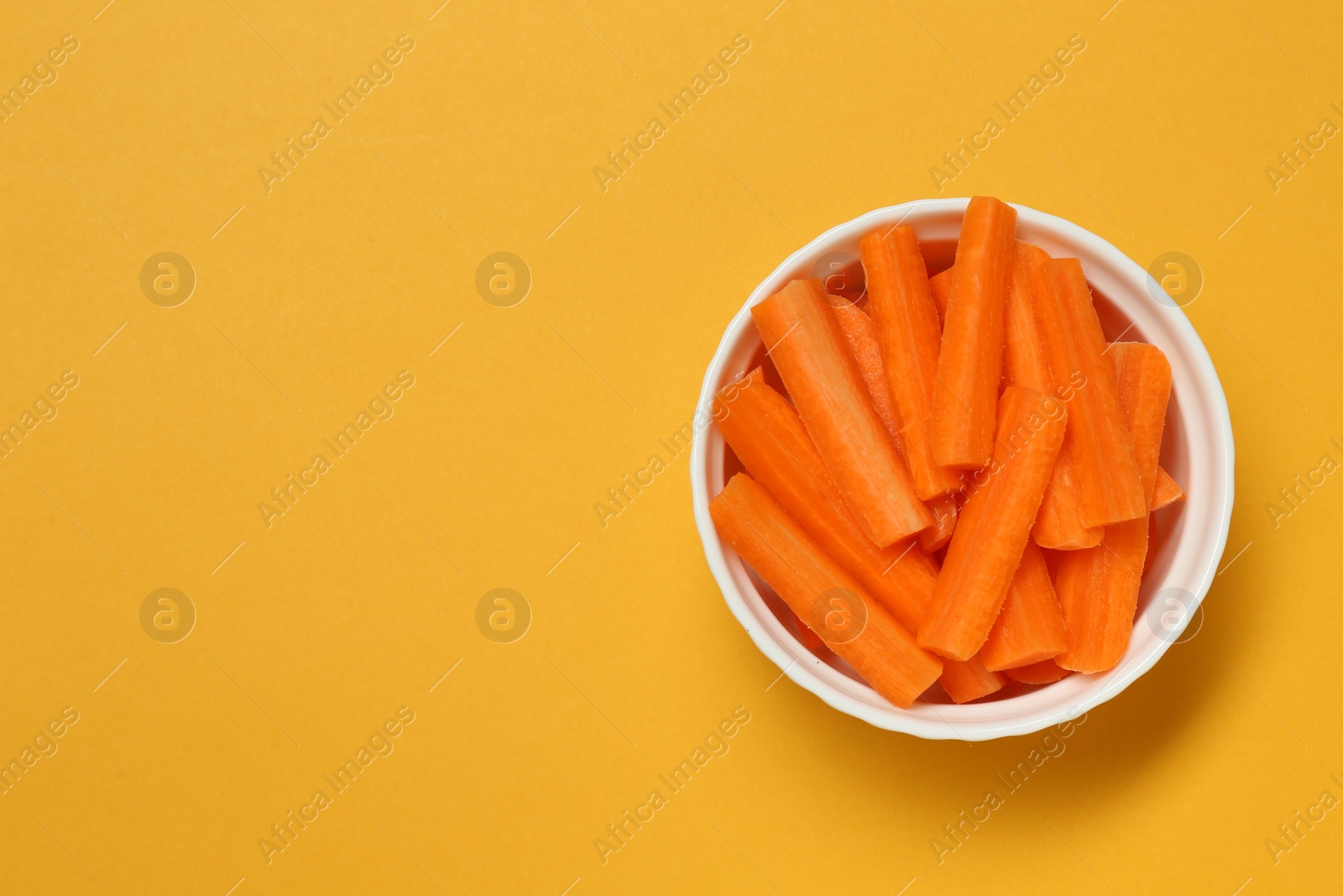 Photo of Cut fresh carrot in bowl and space for text on orange background, top view. Finger food