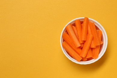Photo of Cut fresh carrot in bowl and space for text on orange background, top view. Finger food