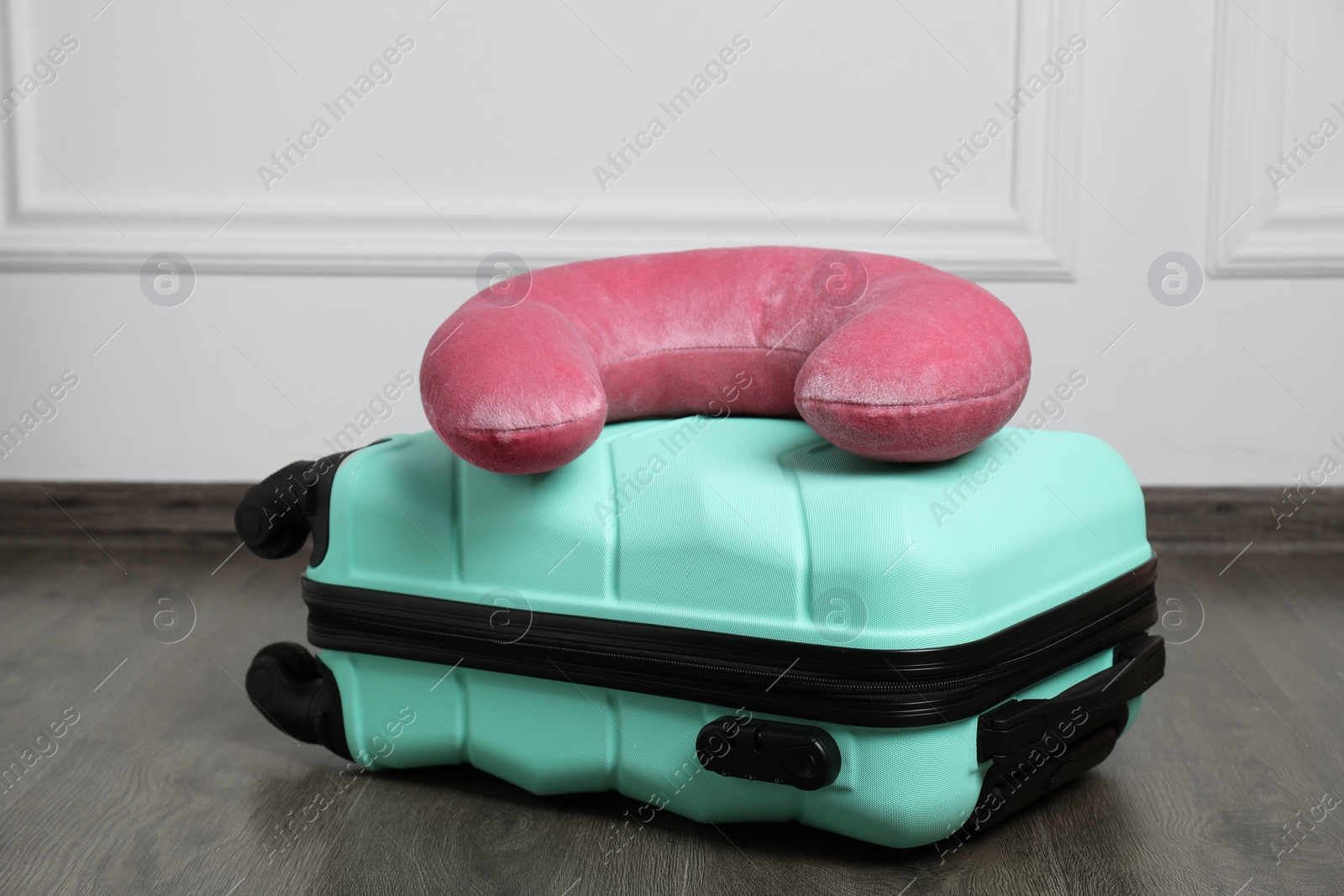 Photo of Pink travel pillow and turquoise suitcase on floor indoors