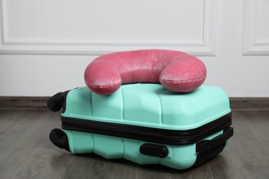 Photo of Pink travel pillow and turquoise suitcase on floor indoors