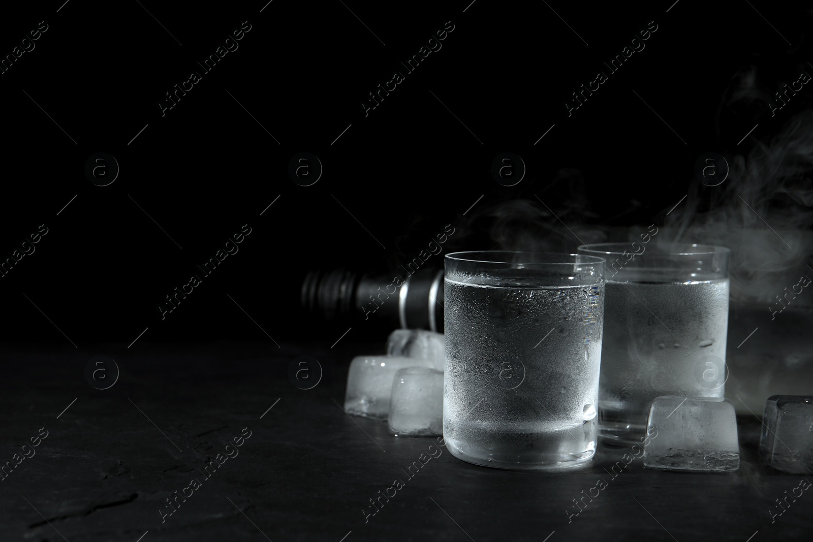 Photo of Vodka in shot glasses with ice on table against black background, space for text