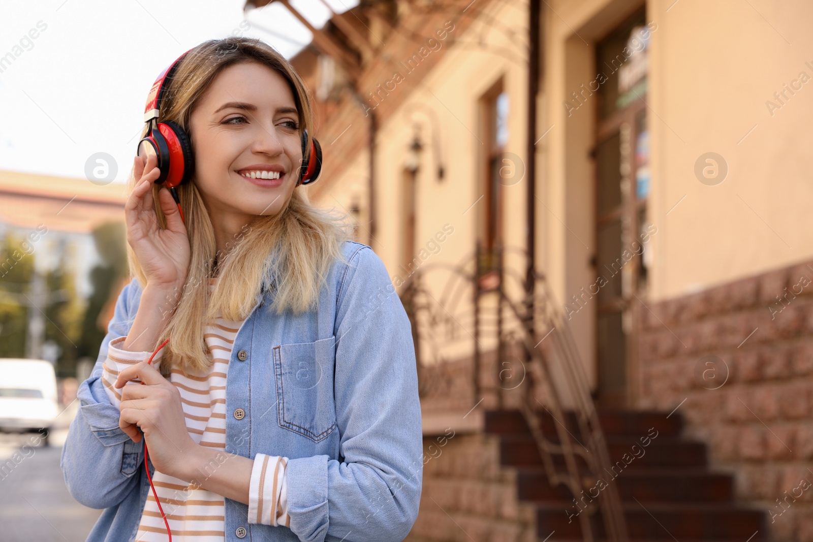 Photo of Happy young woman with headphones listening to music on city street