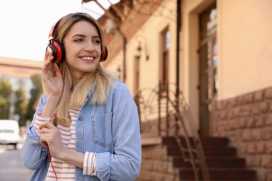 Photo of Happy young woman with headphones listening to music on city street