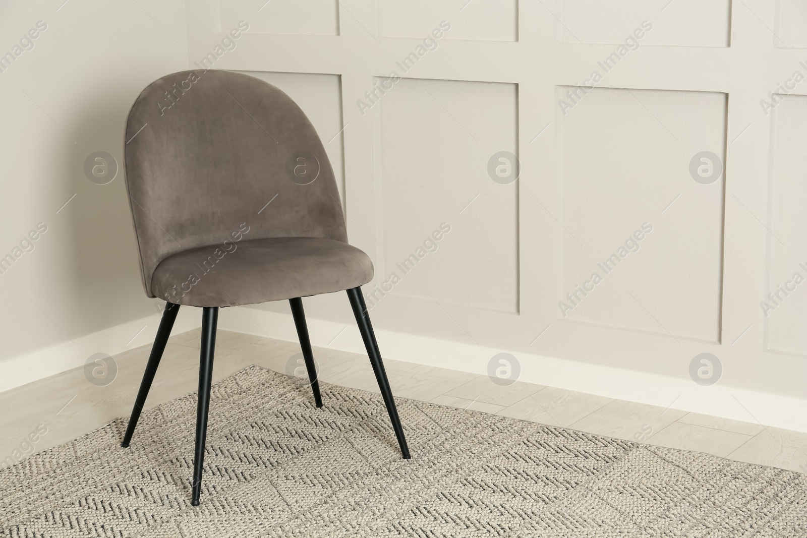 Photo of Stylish grey chair near light wall in room. Space for text
