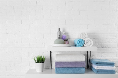 Photo of Shelves with clean towels and toiletries on brick wall. Space for text