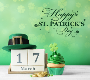 Image of Decorated cupcake, wooden block calendar, hat and coins on white table. St. Patrick's Day celebration