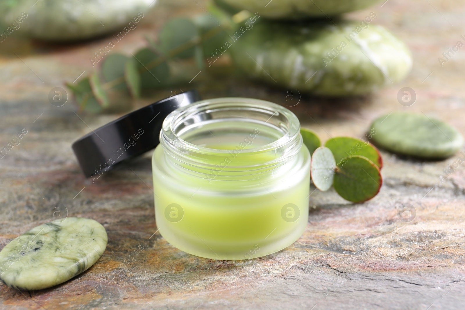 Photo of Jar of cream, spa stone and eucalyptus leaves on textured table, closeup. Body care product