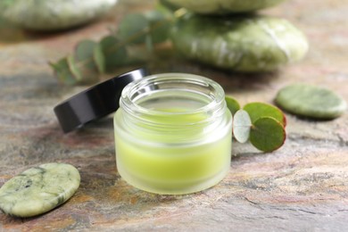 Photo of Jar of cream, spa stone and eucalyptus leaves on textured table, closeup. Body care product