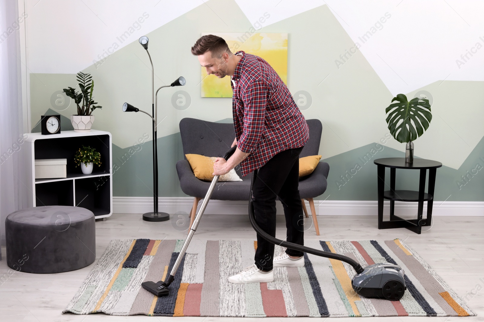 Photo of Young man removing dirt from carpet with vacuum cleaner at home