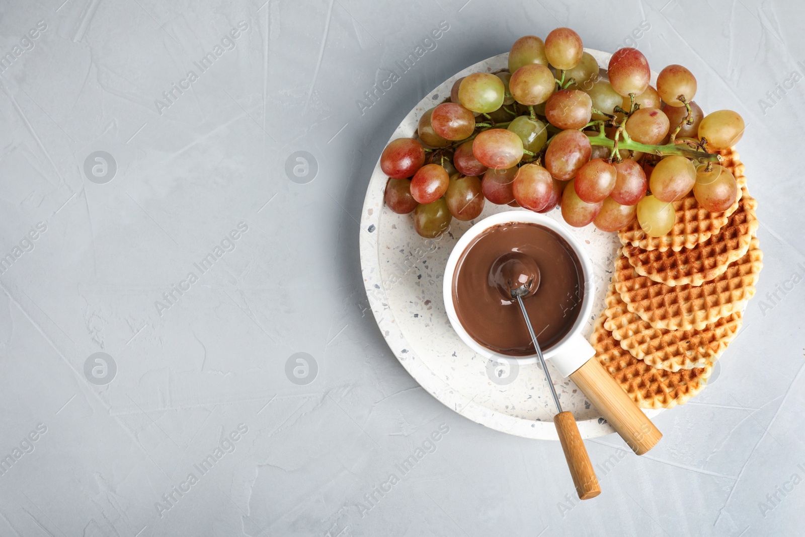 Photo of Fondue pot with chocolate and grape on grey table, top view. Space for text