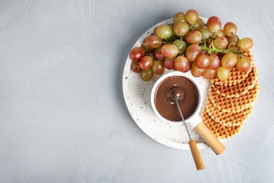 Photo of Fondue pot with chocolate and grape on grey table, top view. Space for text